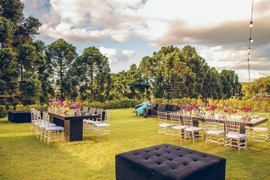 Gramado com mesas e lounge montados, cercado de araucárias